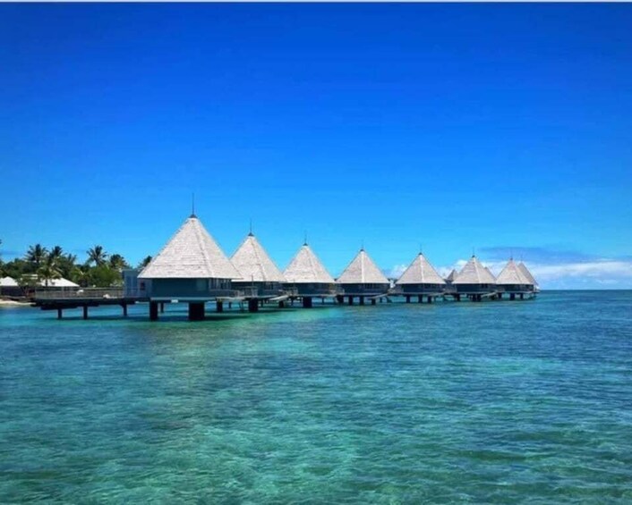 Overwater bungalows with thatched roofs on stilts in clear turquoise water. 2