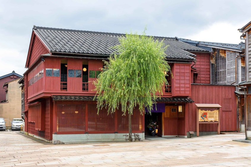 A traditional red wooden building with a tiled roof, a hanging willow tree, and a stone-paved street. 3