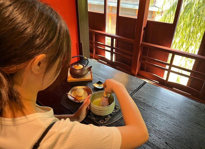 A person sitting at a table with a teapot, a cup, and a bowl, likely preparing or serving tea. 4