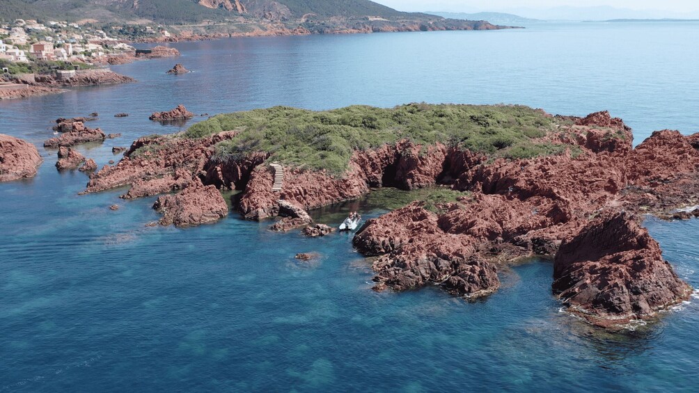 A rocky island surrounded by clear blue waters, with a small group of people on a boat near the shore. 4