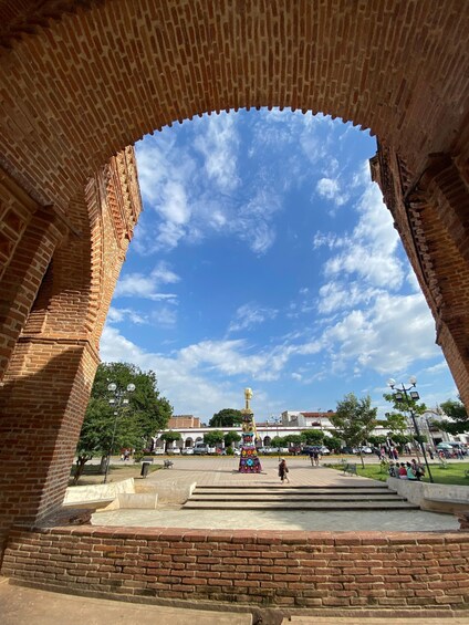 A brick archway with a clear blue sky and a statue in the plaza below. 3
