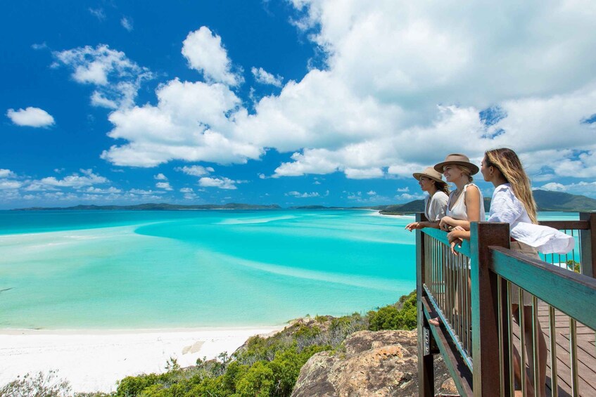 A coastal landscape with turquoise waters, a sandy beach, and a wooden viewing platform. 1