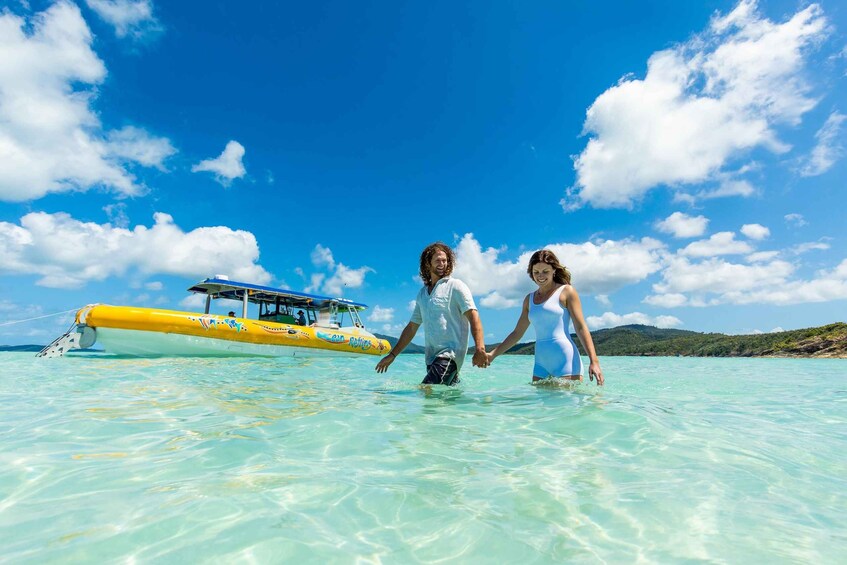 A couple walking in shallow turquoise water with a yellow boat in the background. 5