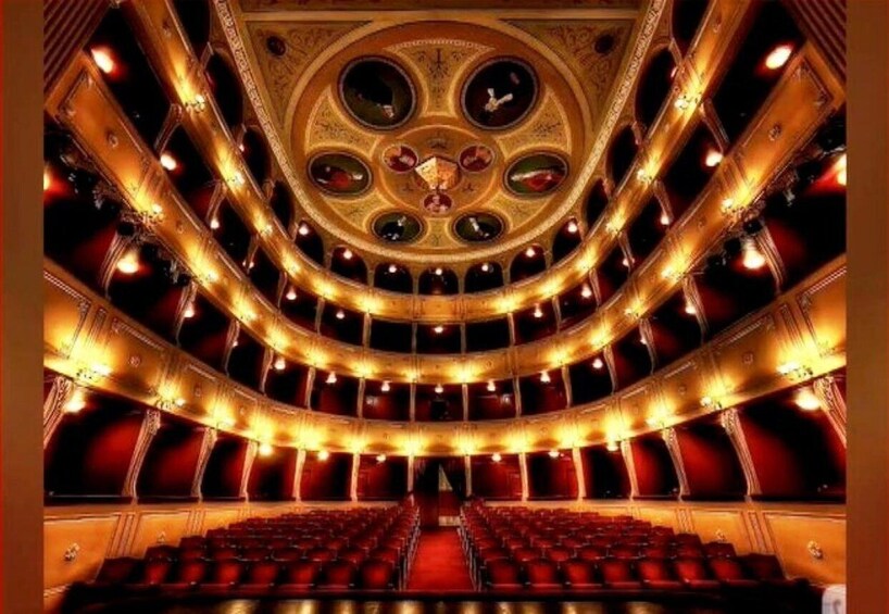A grand theater with ornate ceiling and red seating. 3