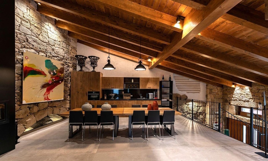 A modern kitchen with wooden beams, stone walls, and a dining area with black chairs. 1