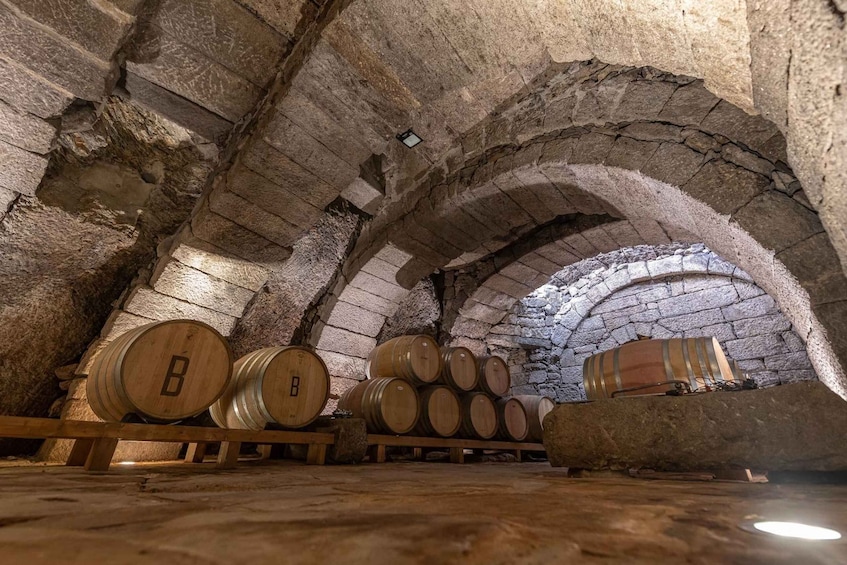 An underground wine cellar with stone arches and wooden wine barrels. 5