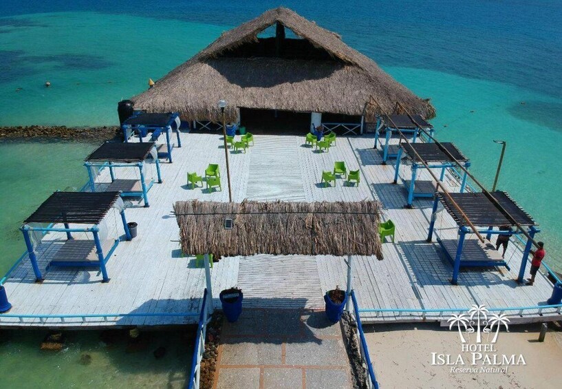 A thatched-roof structure with a wooden deck, green chairs, and a blue railing. 1