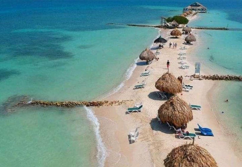 A beach with thatched umbrellas, lounge chairs, and a clear blue sea. 2
