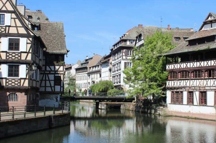 A river with traditional half-timbered houses, a bridge, and a clear blue sky. 4