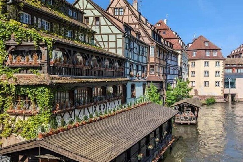 A riverside town with traditional half-timbered buildings, a wooden boat docked by the water, and a small covered structure. 5