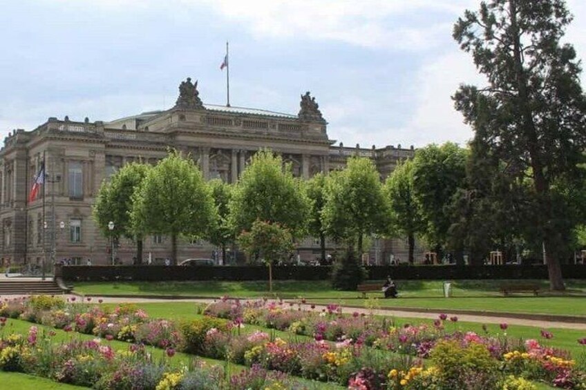 A large historic building with a flag, surrounded by a well-maintained garden with various flowers. 2