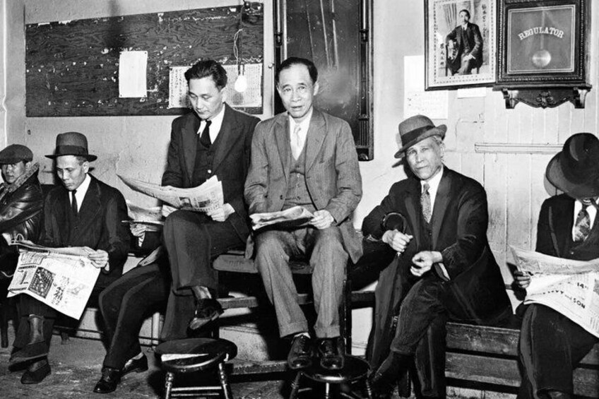 A group of men sitting on benches, reading newspapers. 3