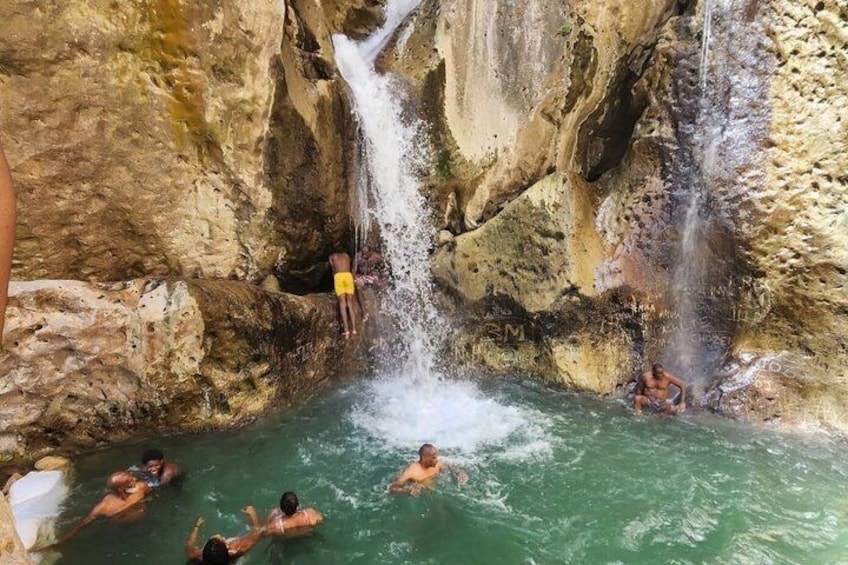 A natural hot spring with multiple waterfalls and people swimming. 1