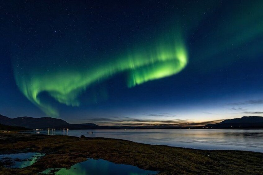 The Northern Lights over a calm lake with distant mountains and a clear night sky. 1