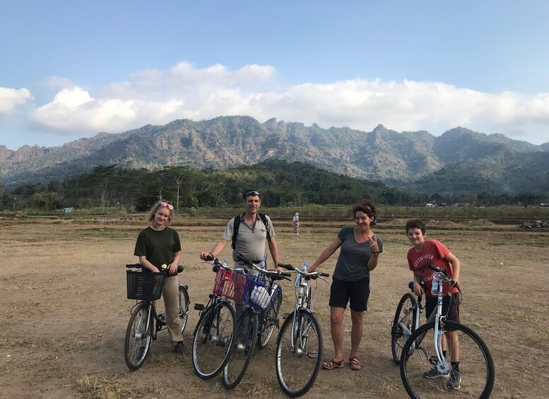A group of people with bicycles in a rural landscape with mountains in the background. 4