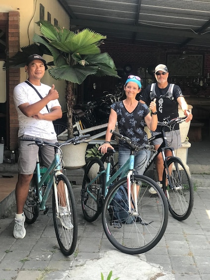 Three people standing next to bicycles in an outdoor setting with a brick wall and a potted plant in the background. 5