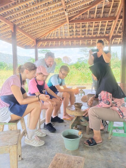 A group of people sitting under a wooden roofed structure, engaged in pottery making. 2