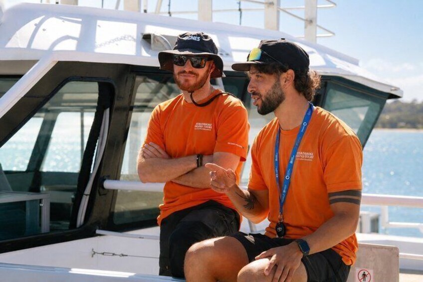 Two people in orange shirts on a boat with a clear sky and water in the background. 4