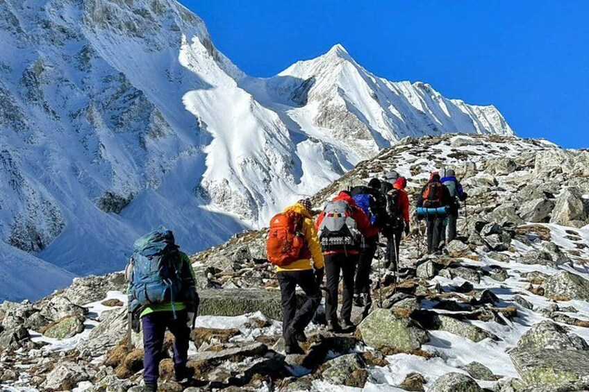 A group of hikers on a rocky mountain trail with snow patches and a snow-capped peak in the background. 3