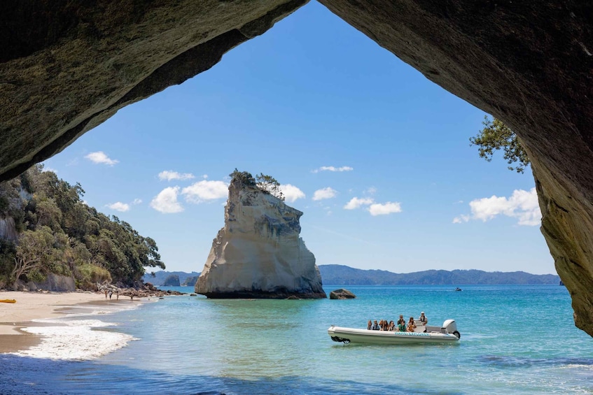 A coastal scene with a large rock formation, clear blue water, and a boat with passengers. 1