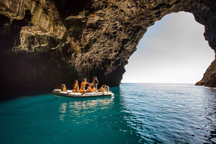 A boat with people wearing life jackets in a clear blue sea, passing through a natural rock arch. 2