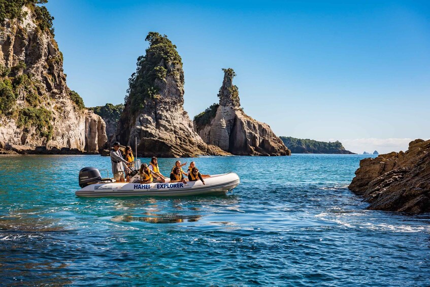A group of people on a boat labeled 'HAHEI EXPLORER' in clear blue waters with rocky cliffs in the background. 4