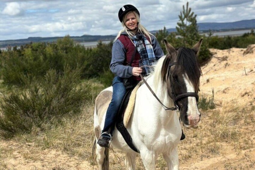 A person riding a white horse with a brown mane and tail on a dirt path surrounded by greenery and hills in the background. 4