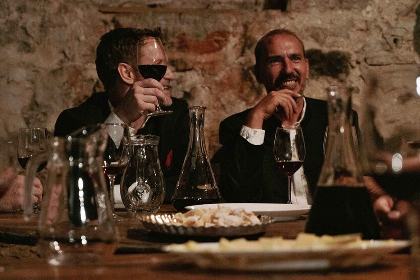 Two people sitting at a table with wine glasses and a bottle of wine. 1