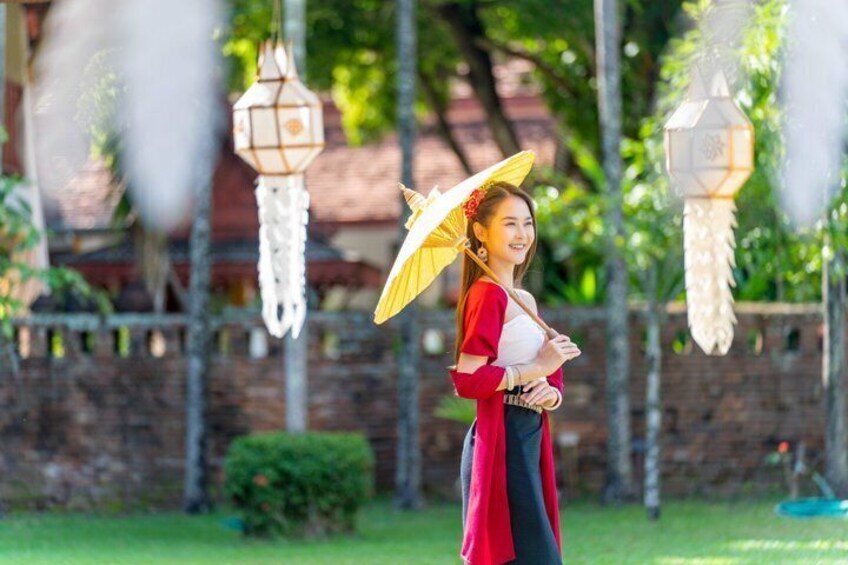A person holding a yellow umbrella, standing in a garden with hanging lanterns. 2