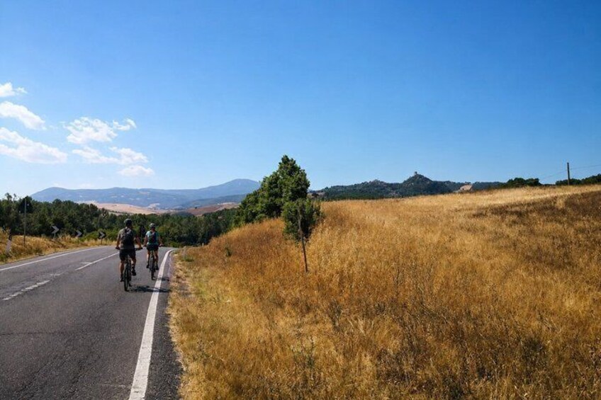 A road with two cyclists, a clear sky, and distant hills. 5