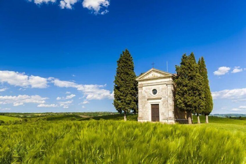A small stone church surrounded by tall trees in a grassy field under a clear blue sky. 2