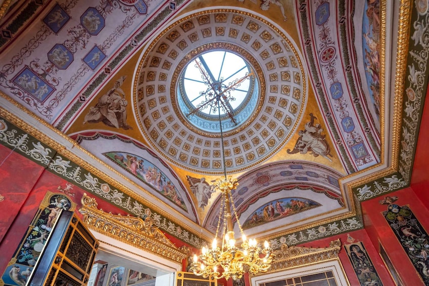 A grand, ornately decorated interior with a large circular skylight, intricate frescoes, and a chandelier. 1