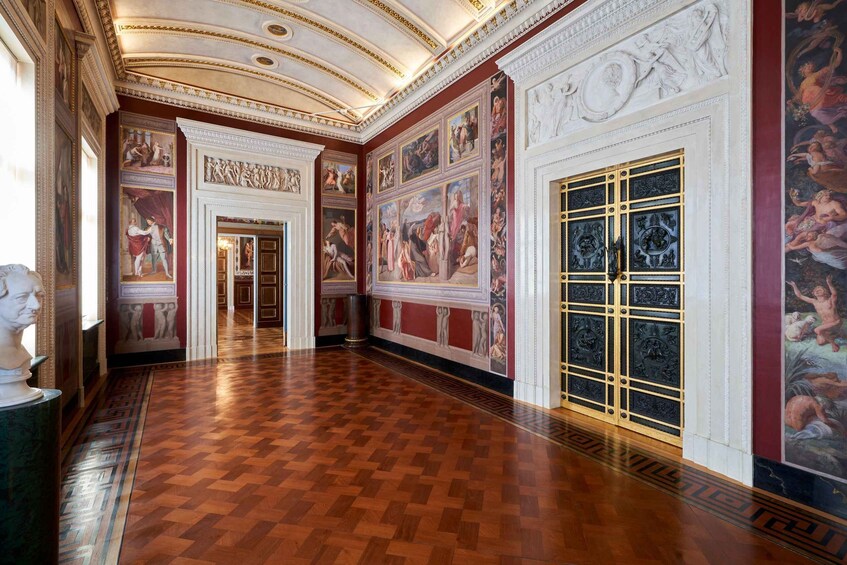 A grand hallway with ornate ceilings, classical paintings, and a large ornate door. 2