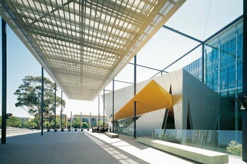 A modern building with a glass facade, a geometric yellow structure, and a grid-patterned ceiling. 5