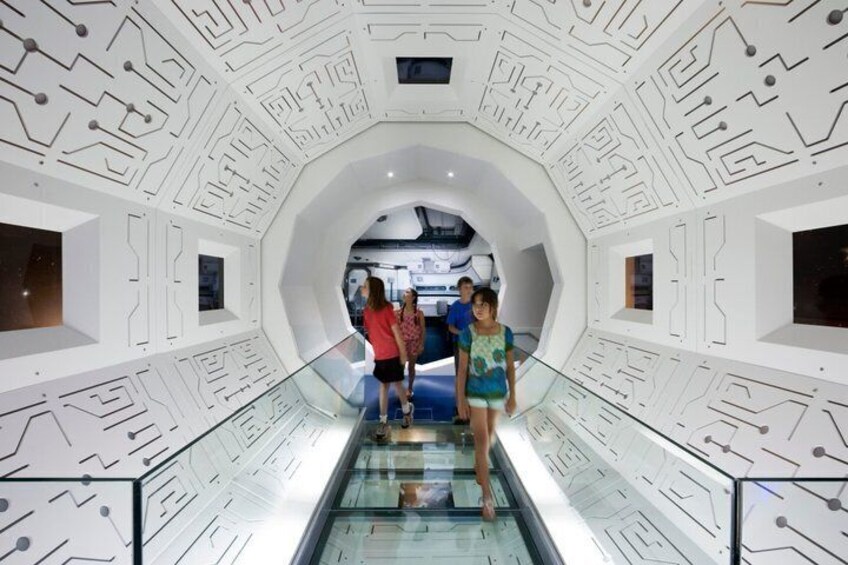A futuristic interior with a curved glass walkway and a white, circuit-like ceiling design. 3