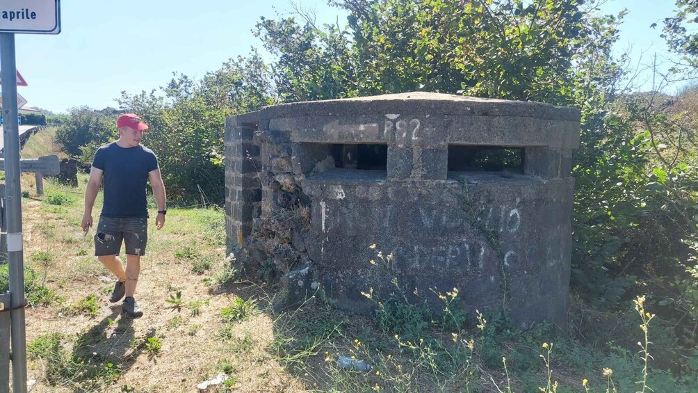A man standing next to a weathered concrete structure with graffiti and a sign that reads 'april'. 4