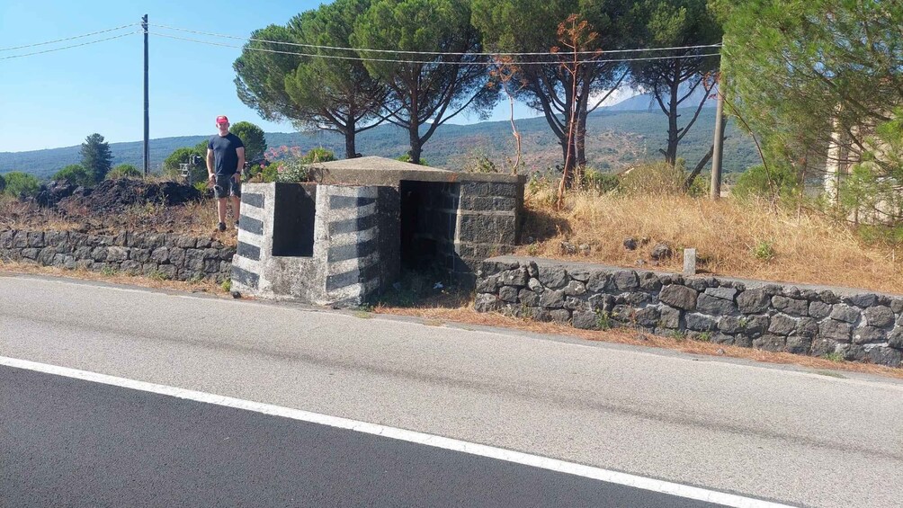 A stone structure near a road with a person standing beside it. 3