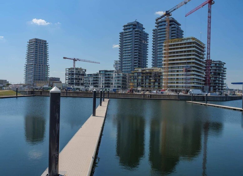 A waterfront with a dock and several high-rise buildings under construction, including a prominent red crane. 3