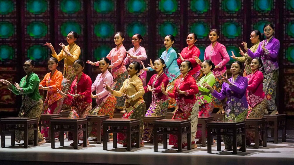 A group of people performing a traditional dance on a stage with a green and black patterned backdrop. 3