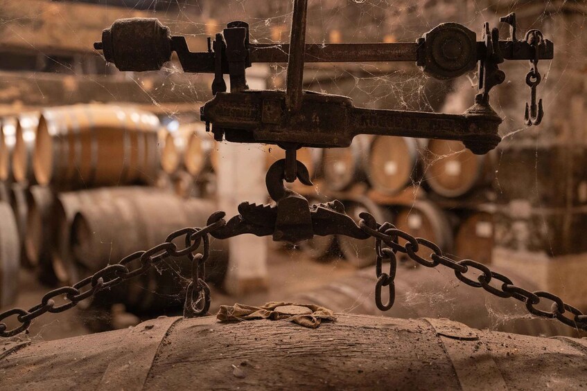 A rusty metal structure with chains, possibly a crane or lifting mechanism, in an industrial setting with barrels in the background. 3