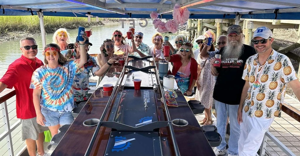 A group of people on a boat with a covered deck, a table with cups and a bottle, and a river in the background. 5