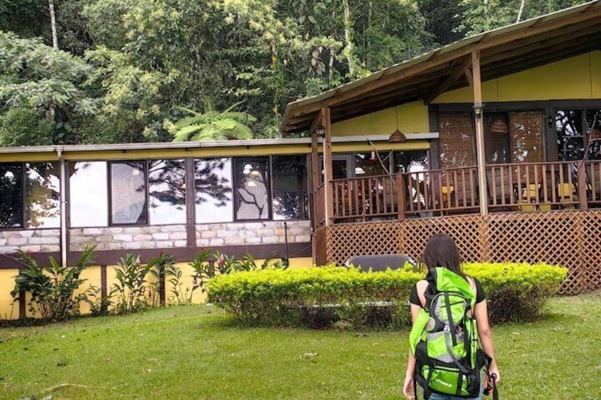 A person with a green backpack walking towards a wooden building with a porch. 5
