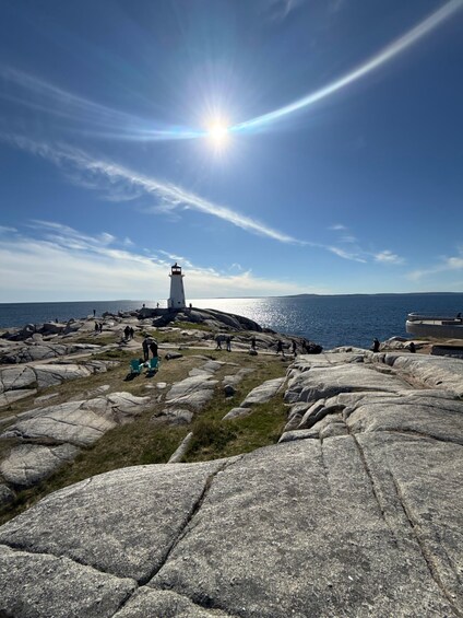 A lighthouse on a rocky coastline with the sun shining brightly in the sky. 1