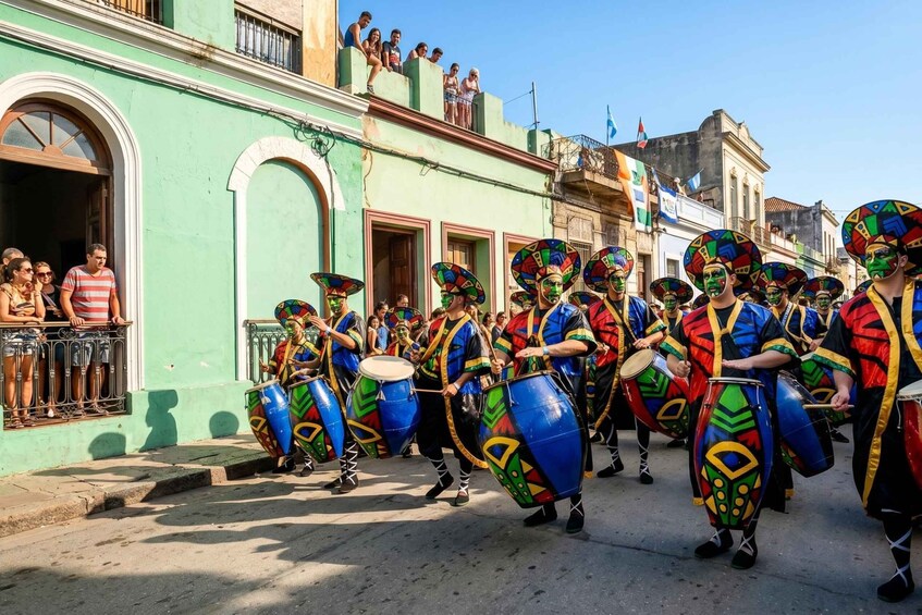 A group of people in colorful costumes and masks, playing drums on a street. 1