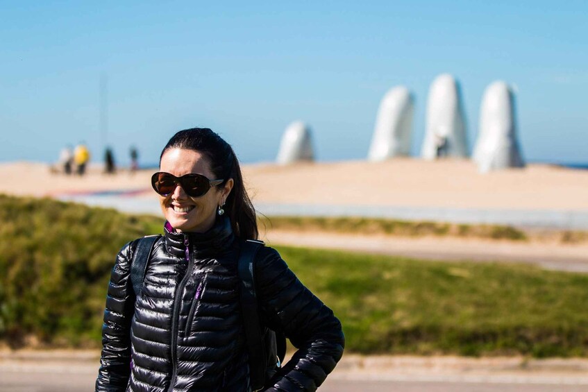 A person standing outdoors with a clear sky, wearing a black jacket, and a landscape with a sandy area and some greenery in the background. 4