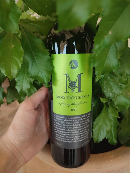 A bottle of Moschato Spinas wine with a green label, held by a hand. 3