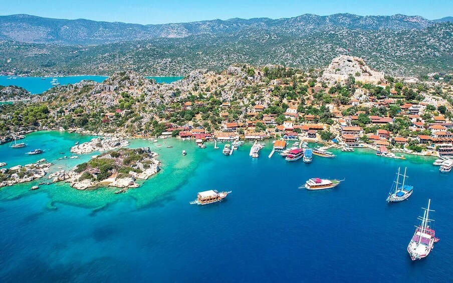 A coastal town with boats docked in turquoise waters, surrounded by hills and a castle. 2