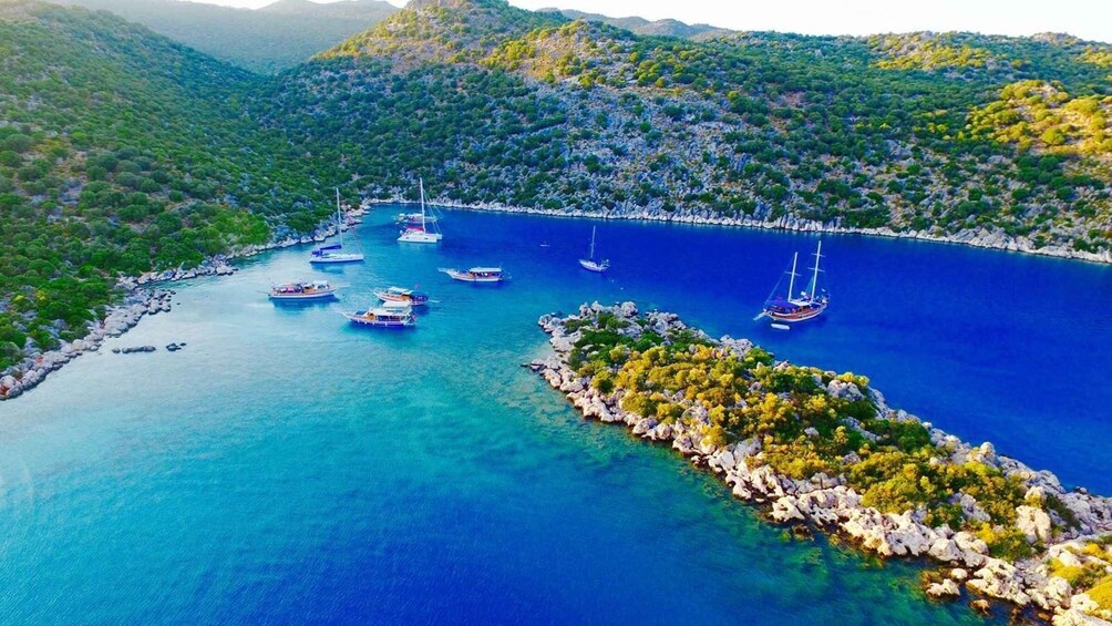 A coastal landscape with boats anchored in a bay surrounded by rocky terrain and dense vegetation. 1