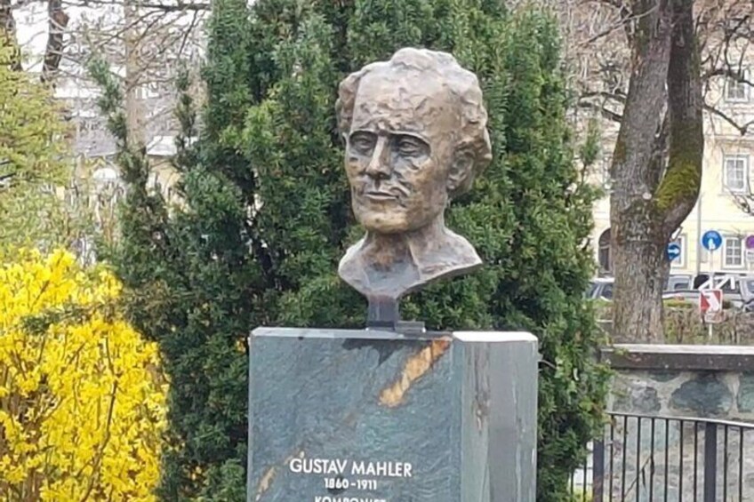 A bust sculpture of Gustav Mahler with a plaque, surrounded by trees and a fence. 3