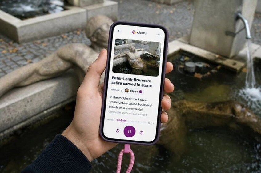 A hand holding a smartphone displaying an article about Peter-Lenk-Brunnen. 1